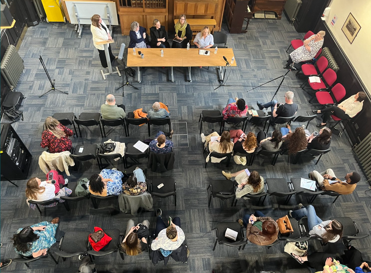 Overhead shot of people sitting in a room listening to a panel of speakers